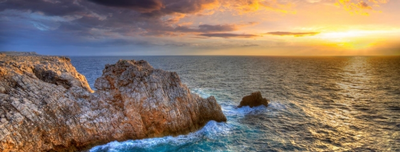 Coucher ou lever de soleil sur la mer avec rochers en premier plan