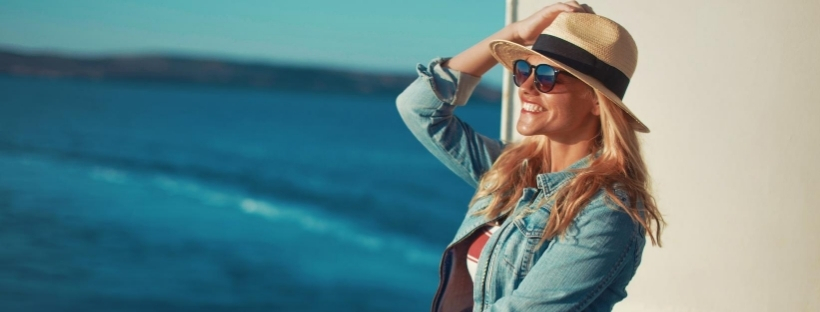 Femme portant un chapeau, lunettes de soleil, veste en jean, regardant la mer