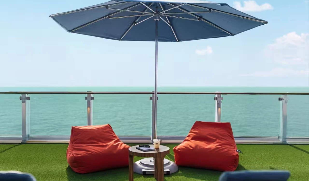 Deux poufs rouges et une table sous un parasol, face à la mer.