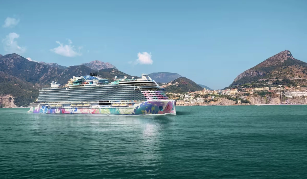 Le paquebot NORWEGIAN BELLA navigue devant une côte montagneuse.