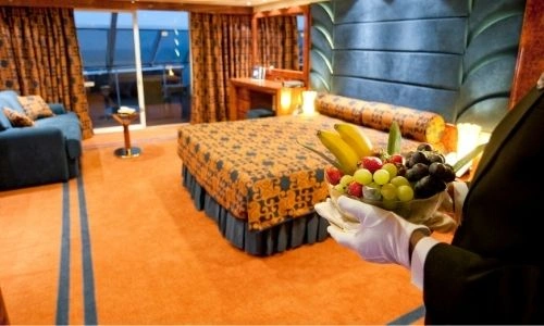 majordome au premier plan qui apporte une corbeille de fruits dans une suite du MSC Yacht Club