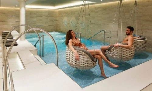 un jeune couple qui se détend dans des fauteuils en osier au dessus d’une petite piscine dans un spa