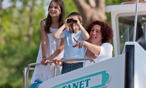 Deux enfants et leur maman qui observent tous trois en direction du même point, le petit garçon observant depuis des jumelles