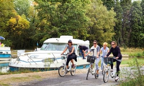famille qui se balade à vélo à côté d’un bateau sans permis sur le bord d’une rivière