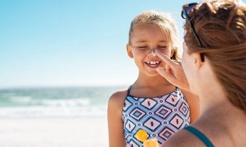 jeune maman qui met de la cr&egrave;me solaire &agrave; sa petite fille tout sourire