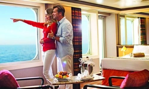 Couple dans leur cabine ext&eacute;rieure, la femme pointe du doigt la mer et l'homme la tiens juste derri&egrave;re