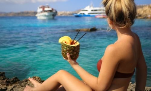 Jeune femme devant la mer qui tient dans ses mains un cocktail ananas