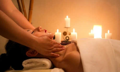 Une femme vue de profil se faisant masser la nuque au spa avec des bougies en arri&egrave;re plan