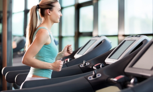 Une femme de profil faisant du sport sur un tapis de course dans une salle de sport