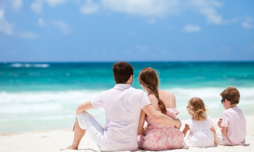 Vue sur une famille de 4 personnes de dos assises sur le sable blanc aux Caraïbes