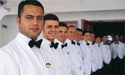  membres de l’équipage d’un bateau alignés, en costume blanc et noeud papillon noir avec le sourire 