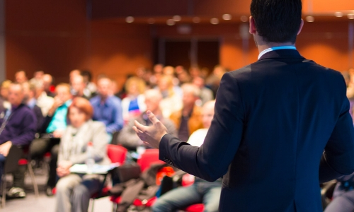 Dans une salle de conférence, personne assises, présentateur debout devant