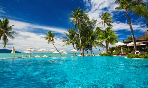 Paysage des Caraïbes, eau turquoise, palmiers, parasols blancs