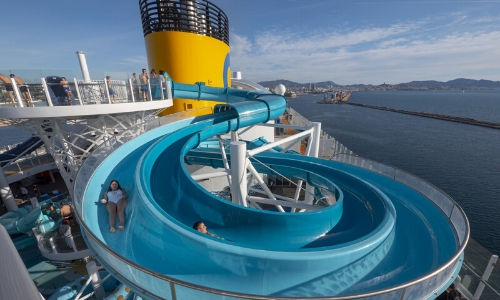 Petite fille glissant sur l'un des toboggans de l'aqua park du Costa Smeralda avec la cheminée jaune Costa en arrière plan