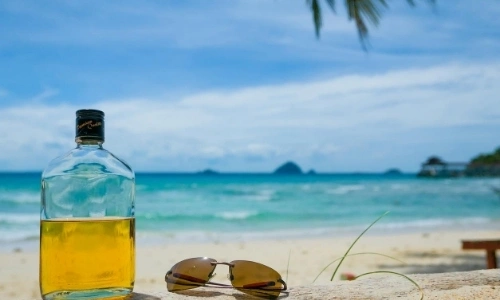 Bouteille de rhum sur une plage de sable blanc, avec lunettes de soleil