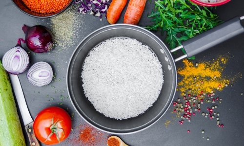 Photo d'un plat pour faire cuire le riz, des oignons coupés, des carottes, une tomate, de la salade et un couteau