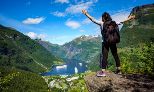 Femme de dos en hauteur, au-dessus d'un fjord, debout et écartant les bras