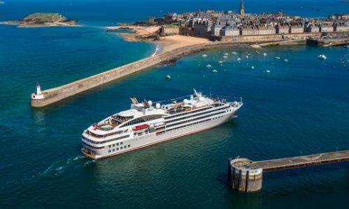 bateau de croisière sur l’eau non loin d’un port, au loin une île avec des habitations 