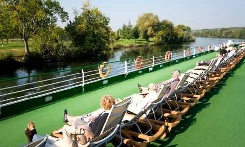 Rangée de passagers qui profitent du soleil sur les transats d'un pont d'un bateau fluvial