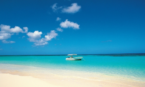 Plage de sable blanc avec eau limpide, ciel bleu et petit bateau