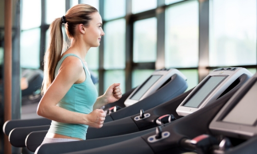 Femme qui fait du sport sur un tapis de course de profil