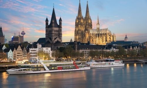 croisière fluviale sur un fleuve au bord d’une ville avec de grands bâtiment dont un clocher illuminé