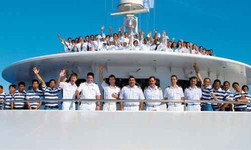 membres de l’équipage qui font des signes de la main, tout sourire en regardant la photo sur le pont supérieur d’un bateau