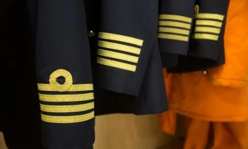 4 uniformes bleu marine d’un équipage rangés dans une armoire, vu sur les manches et les distinctions (bandes dorées et boucle)