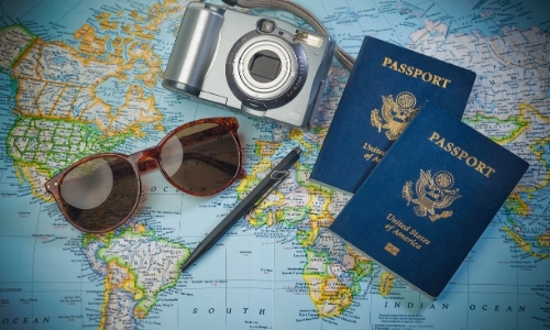 Carte du monde sur laquelle se trouvent un appareil photo, 2 passeports, une paire de lunettes de soleil et un stylo