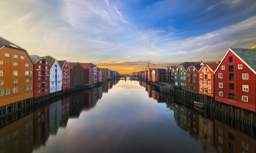 Trondheim au coucher du soleil avec petites maisons en bois de couleurs rouge, jaune moutarde, blanche et marron, avec rivière au milieu