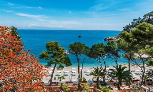 Vue en arrivant sur la plage à Taormine, avec arbres, transats, parasols