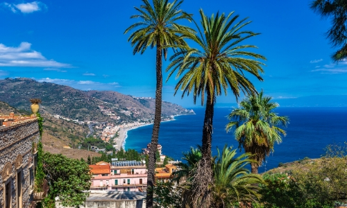 Vue sur la mer depuis Taormine avec palmiers, habitations et montagnes