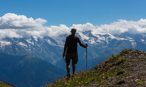 Homme de dos, au sommet d'une montagne, montagnes enneigées au loin