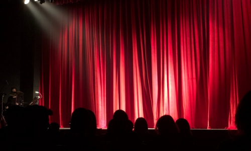 Dans une salle de spectacle, vue sur une scène avec rideau rouge, projecteurs 