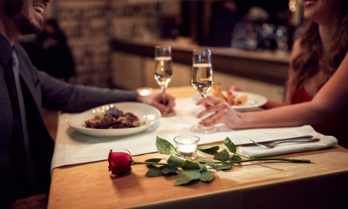 Couple autour d'une table, verre de vin à la main, plats sur la table