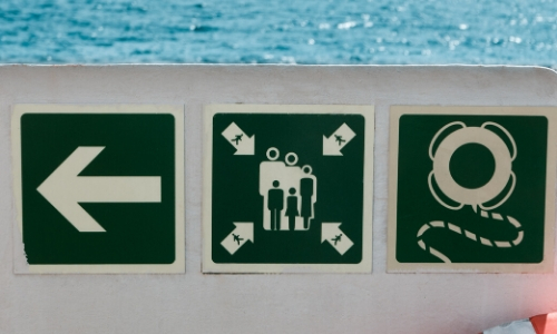 Signalétique sur un bateau de croisière, flèche montrant une direction, pictogramme présentant le point de rassemblement et bouées de sauvetage