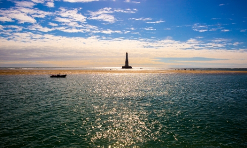 Vue sur l'estuaire de la Gironde avec phare en arrière-plan et un petit bateau naviguant