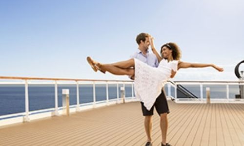 jeune couple sur le pont d’un bateau, l’homme porte sa conjointe dans les bras, qui elle tend et les jambes et les bras en lui souriant 