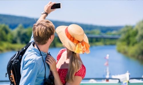 jeune couple de dos, l’homme tend son bras avec son téléphone dans la main pour prendre un selfie de lui et sa compagne