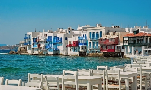 Maisons construites au bord de l'eau, comme sur le fil de l'eau en arrière-plan et tables avec chaises blanches au premier plan