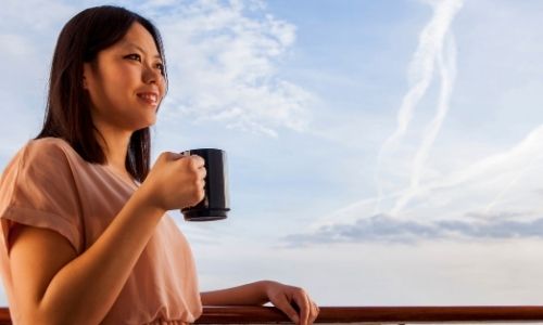 jeune femme qui regarde l’horizon à la barre d’un bateau, une tasse de café à la main