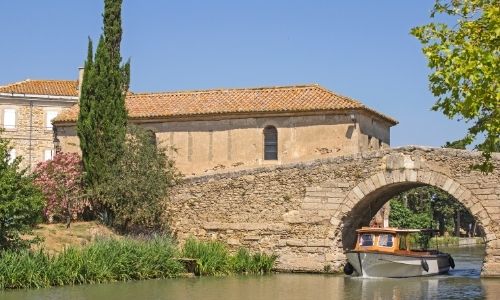 Le village du Somail et son pont à voûte en pierre franchi par une vedette