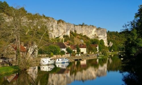 Village de Merry-sur-Yonne et le rocher de Saussois, des bateaux sont amarrés à la berge.