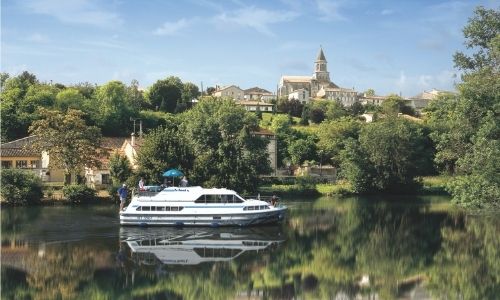 Un bateau sans permis qui navigue sur la rivière de la Charente, on aperçoit dans l’arrière plan une belle église