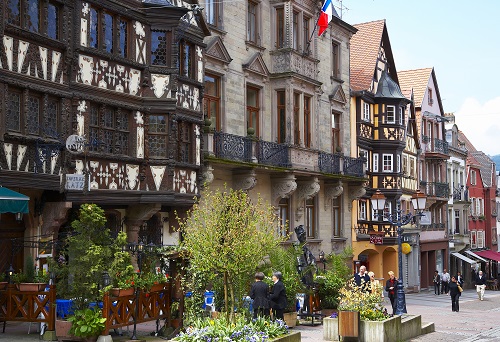 Rangée de maisons alsaciennes à colombages, des touristes les observent depuis la rue piétonne