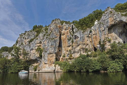 Un bateau de la compagnie Nicols vogue sur le Lot, l'immense falaise en arrière plan couvre quasiment toute la photo