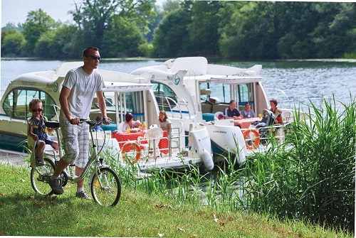 Un père et son fils font une balade à vélo tandis que le reste de la famille est sur deux bateaux au second plan