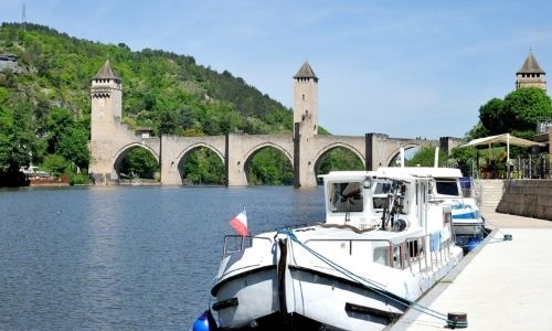 Le Pont Valentré et ces 3 tours dominent le Lot. Au premier plan est amarré deux bateaux de plaisance.