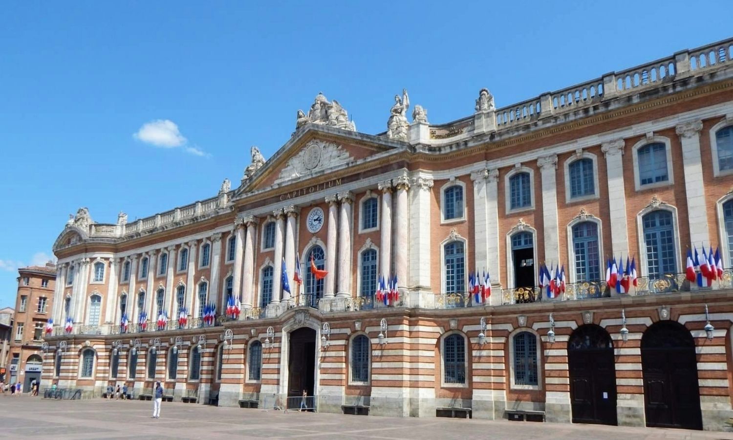 Façade du Capitole arborant des drapeaux français, la photo est prise en bié 