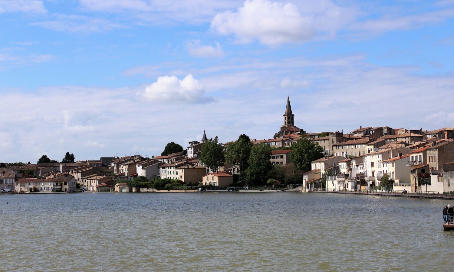 L’étendue d’eau du grand bassin de Castelnaudary s’étend jusqu’aux maisons de la ville. Son église culmine au-dessus des habitations.